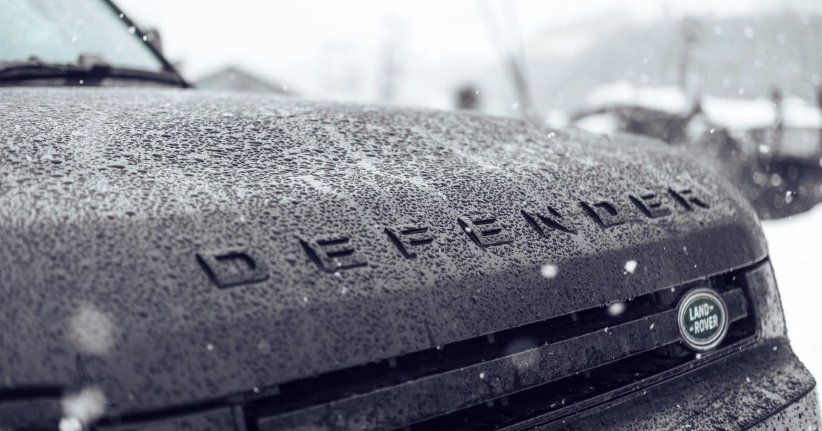 Frost and rain covering the hood of a Land Rover Defender, with its badge and grille visible in cold weather