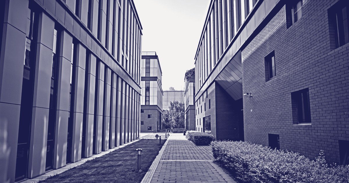 A paved walkway between modern office buildings with glass and brick facades, in a blue-toned photograph