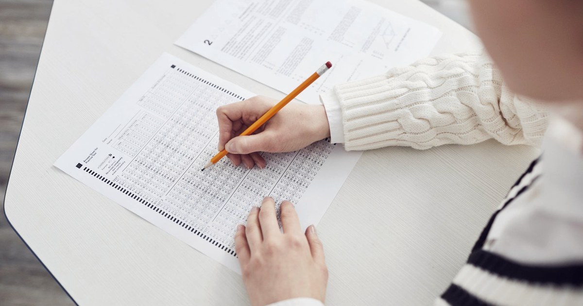 A close-up of a hand filling in an OMR bubble answer sheet with a pencil