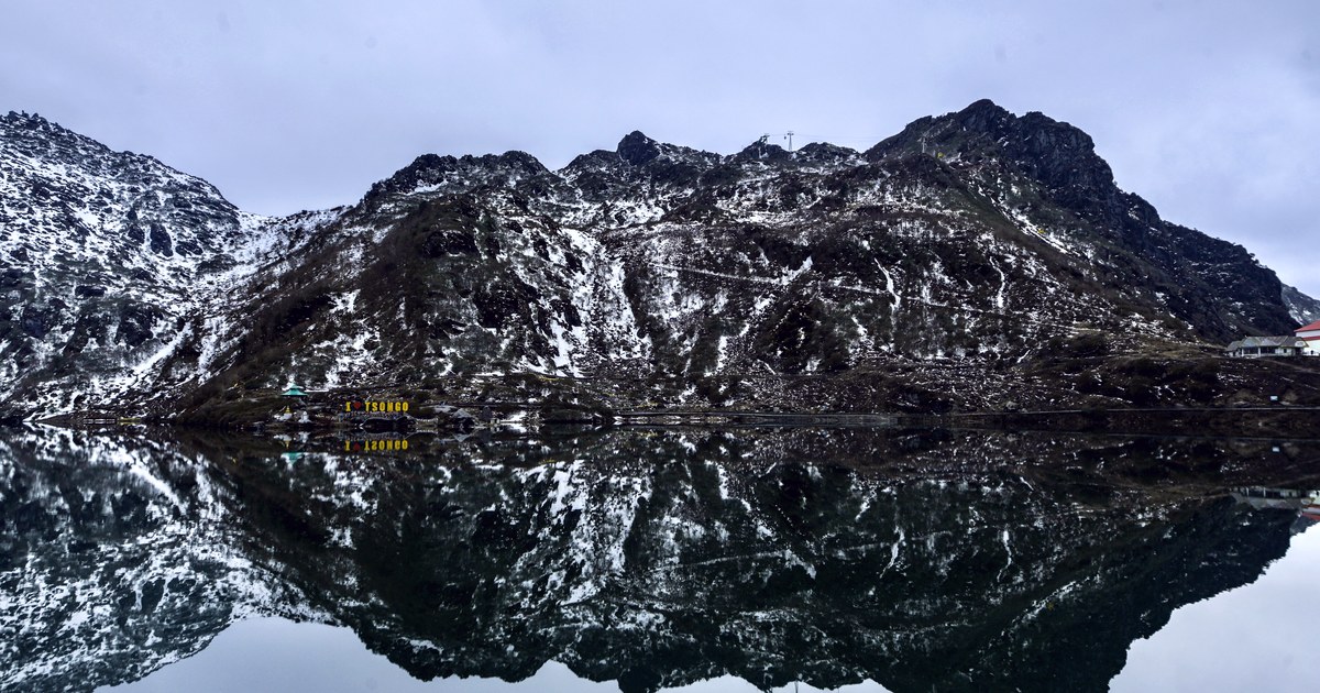 Snow-covered Himalayan mountains reflected in the still, dark water of Tsomgo Lake, a high-altitude glacial lake in Sikkim, India