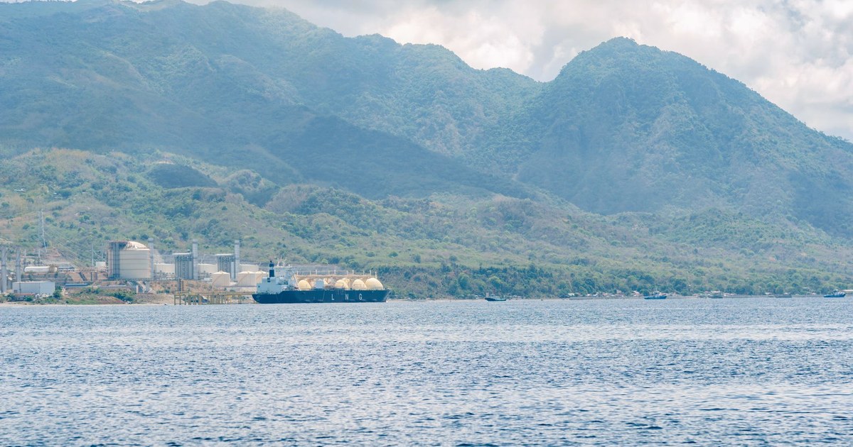 An LNG tanker moored at a gas terminal on a mountainous coastline under a cloudy sky