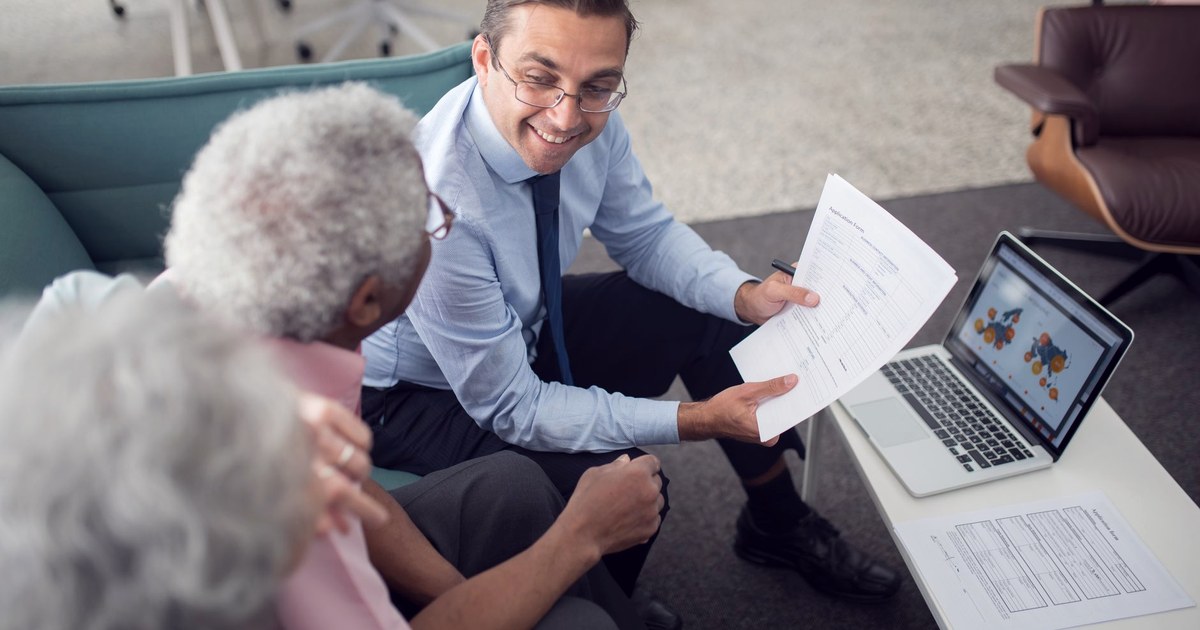 An insurance advisor presenting a policy application form to an elderly couple in an office setting