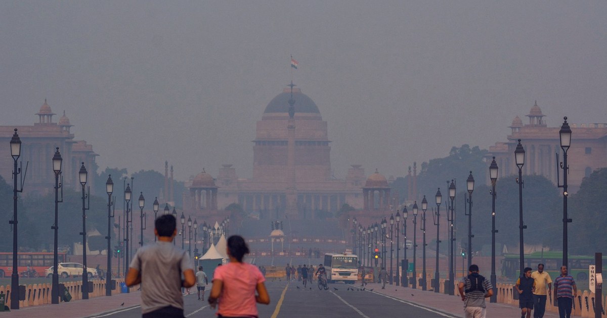 Joggers and pedestrians walking toward a smog-shrouded Rashtrapati Bhavan in New Delhi at dawn
