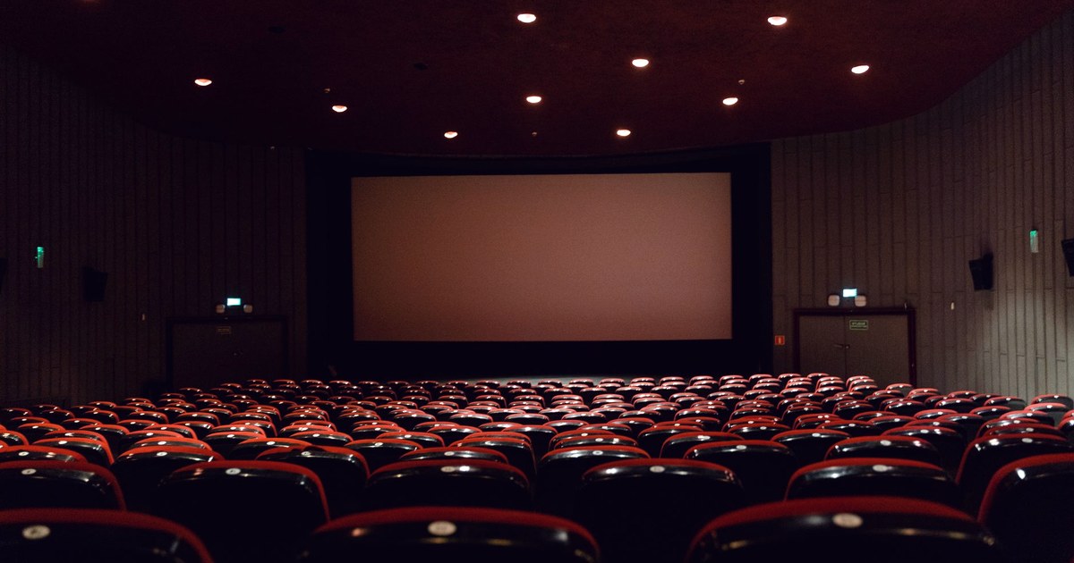 An empty multiplex cinema hall with rows of red and black seats facing a blank projector screen