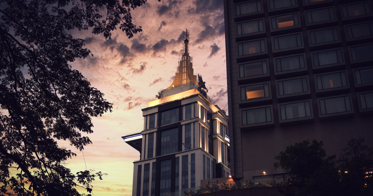 A high-rise office tower lit gold at dusk against a purple and orange Indian city skyline