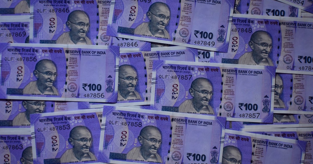 A dense fan of Indian 100 rupee banknotes bearing the Reserve Bank of India name and Mahatma Gandhi portrait, laid out and overlapping