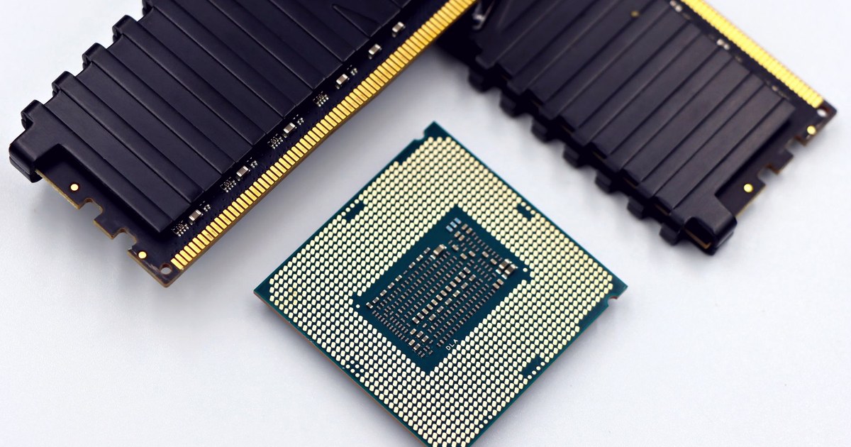 A computer processor chip resting on a white surface next to two black RAM memory modules with gold connector pins