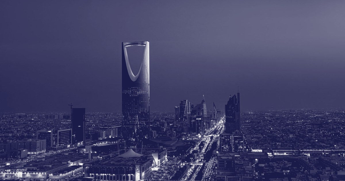 The Kingdom Centre Tower rising above Riyadh's skyline at night, with the city's lit streets and traffic below