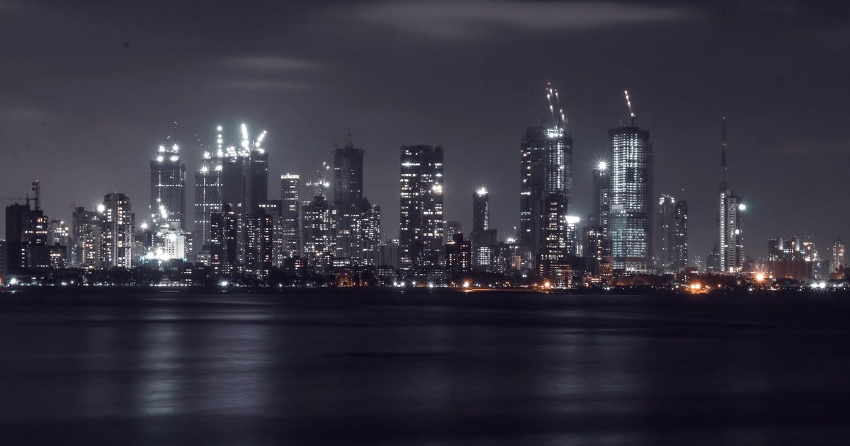 Mumbai's financial district skyline lit up at night, seen across the water, with several skyscrapers under construction