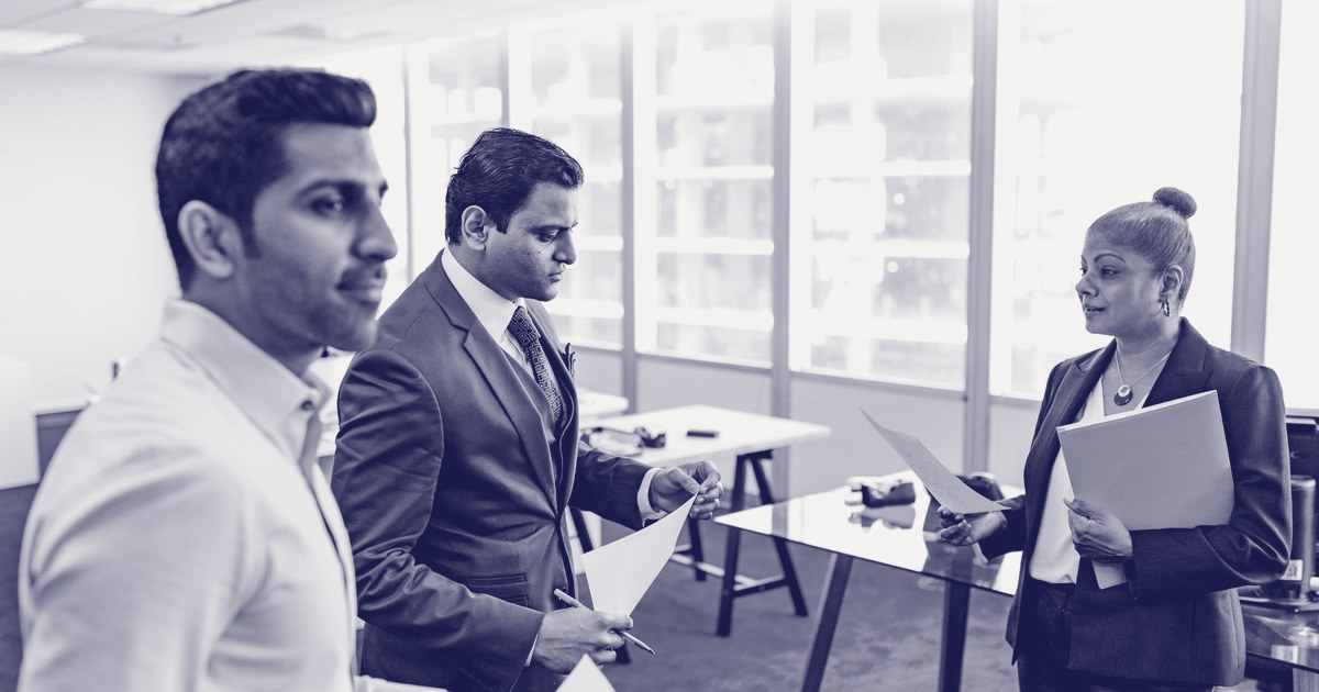 Three financial professionals exchanging documents in a modern office