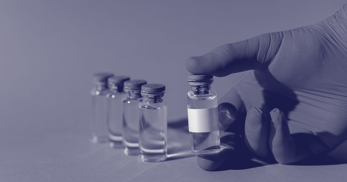 A gloved hand lifting a vaccine vial with a blank label from a row of identical vials