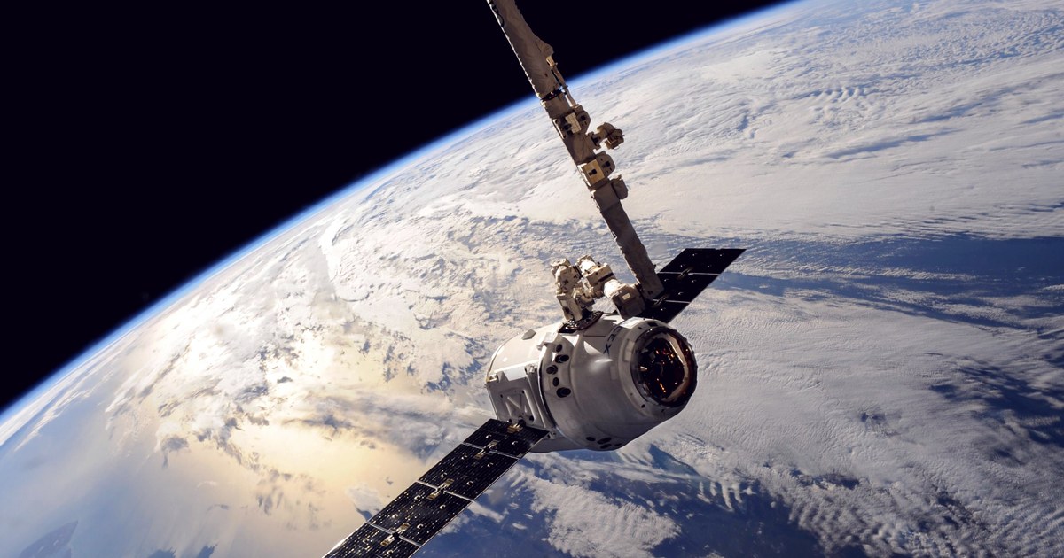 A cargo capsule held by the International Space Station's robotic arm, orbiting above Earth's cloud-covered surface