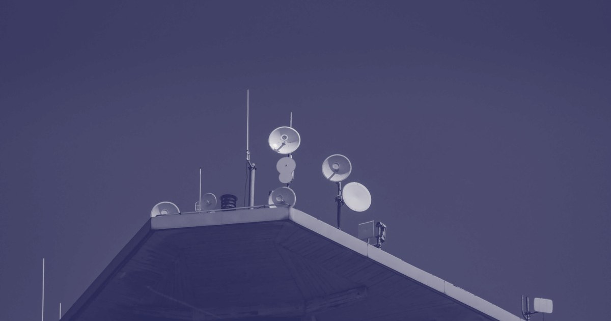 White satellite and microwave dishes mounted on a rooftop against a clear blue sky