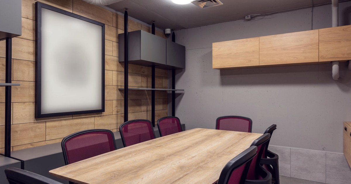 An empty corporate boardroom with a long wooden table and burgundy mesh chairs, no one present