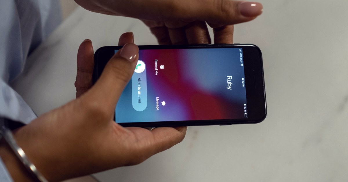 A hand holding a smartphone displaying an incoming call screen with a slide-to-answer prompt