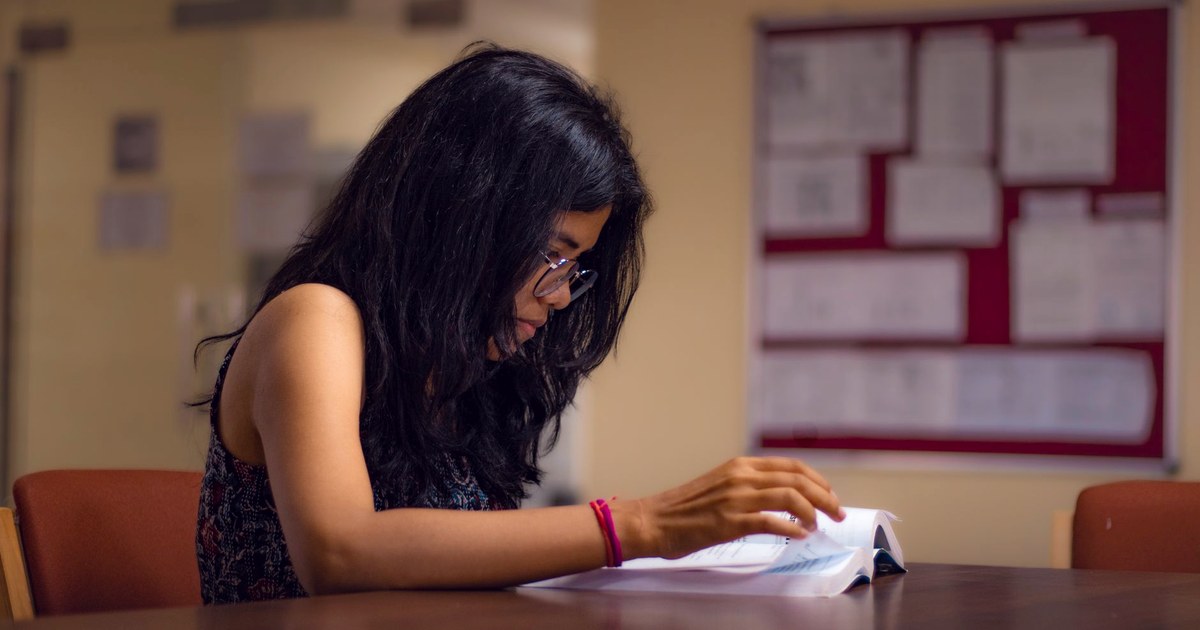A young woman studying from a textbook at a library table in New Delhi