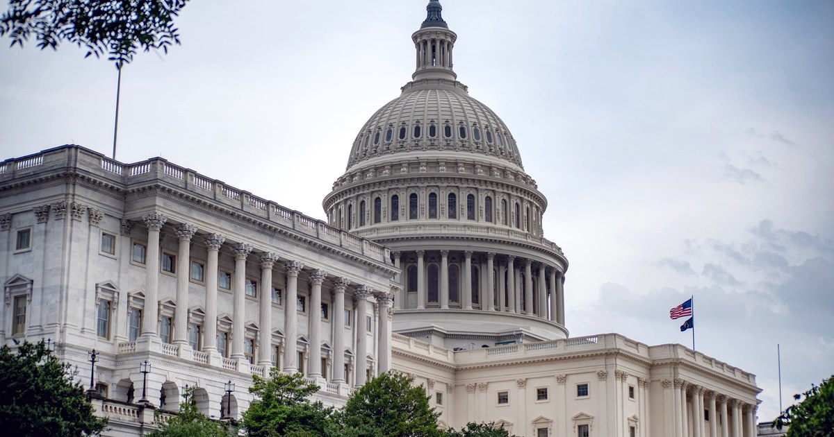 The dome and a wing of the United States Capitol in Washington with an American flag, under a cloudy sky