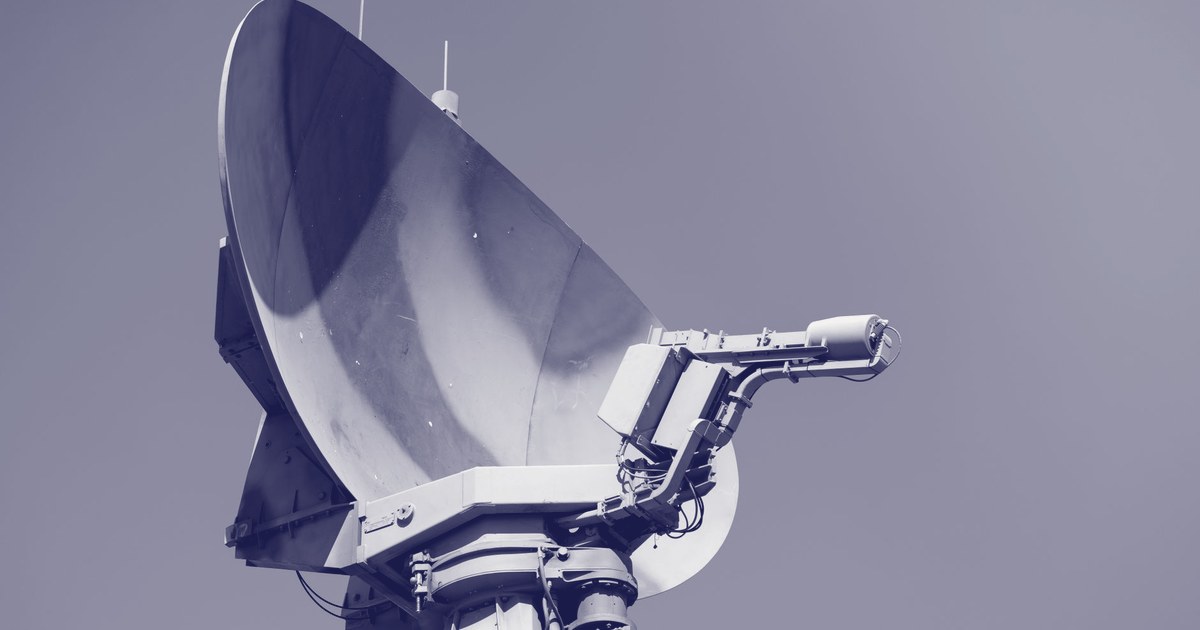 A military tracking radar dish mounted on a mobile platform, angled skyward against a clear sky