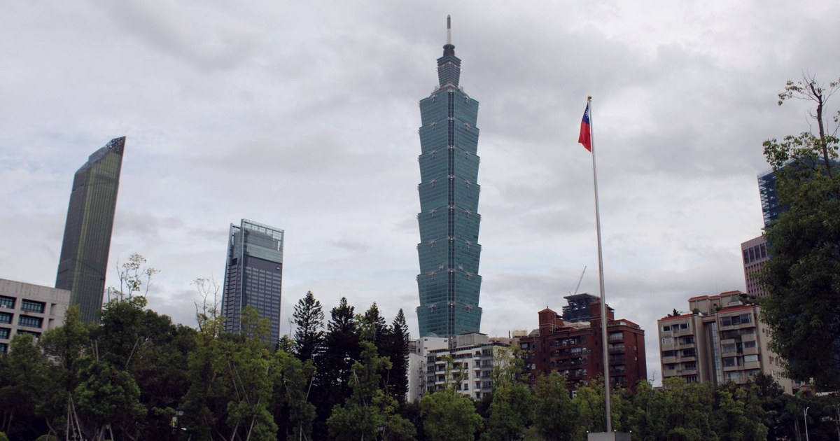 The Taipei 101 skyscraper rising above central Taipei's skyline with Taiwan's flag flying in the foreground under an overcast sky